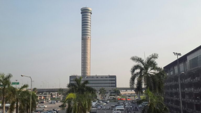 Air traffic control tower at Bangkok Suvarnabhumi Airport rising above palm trees and the airport car park