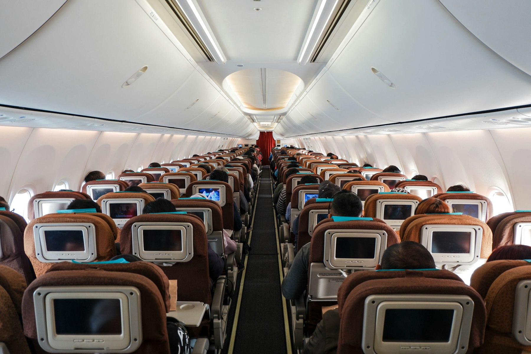 Rows of economy seats with seatback screens inside a passenger aircraft cabin