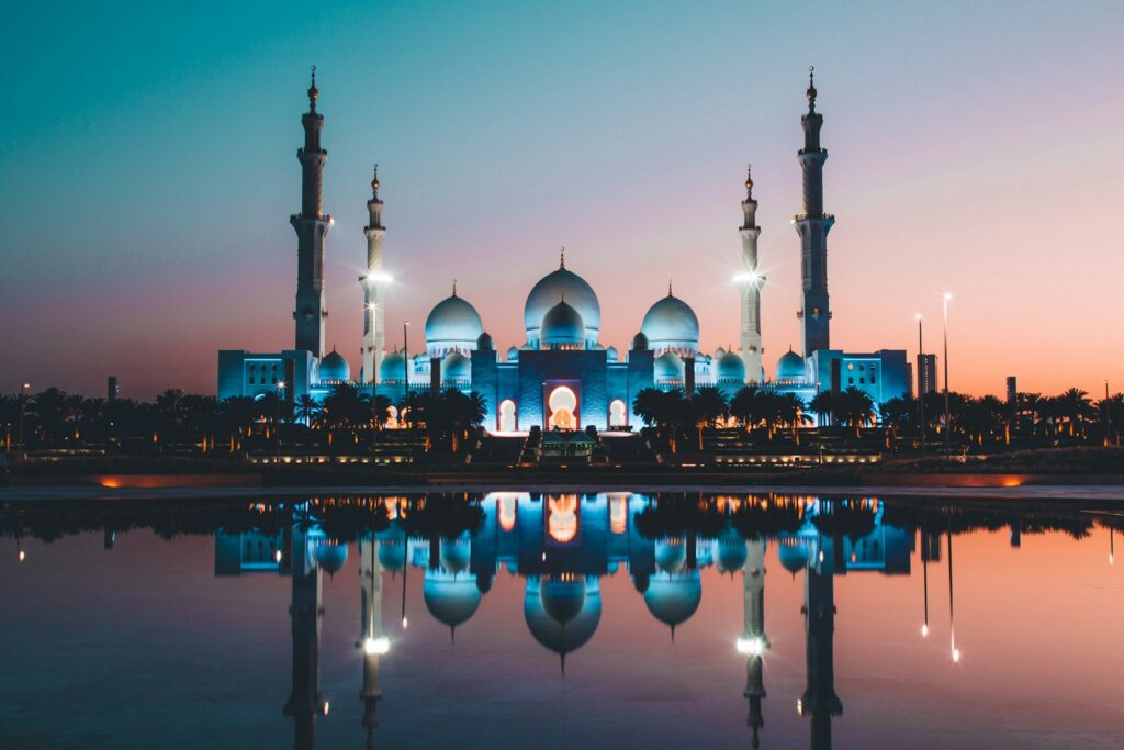 Sheikh Zayed Grand Mosque in Abu Dhabi lit up at dusk and reflected in a pool