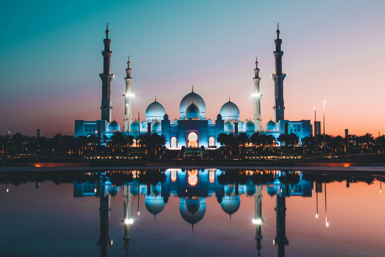 Sheikh Zayed Grand Mosque in Abu Dhabi lit up at dusk and reflected in a pool