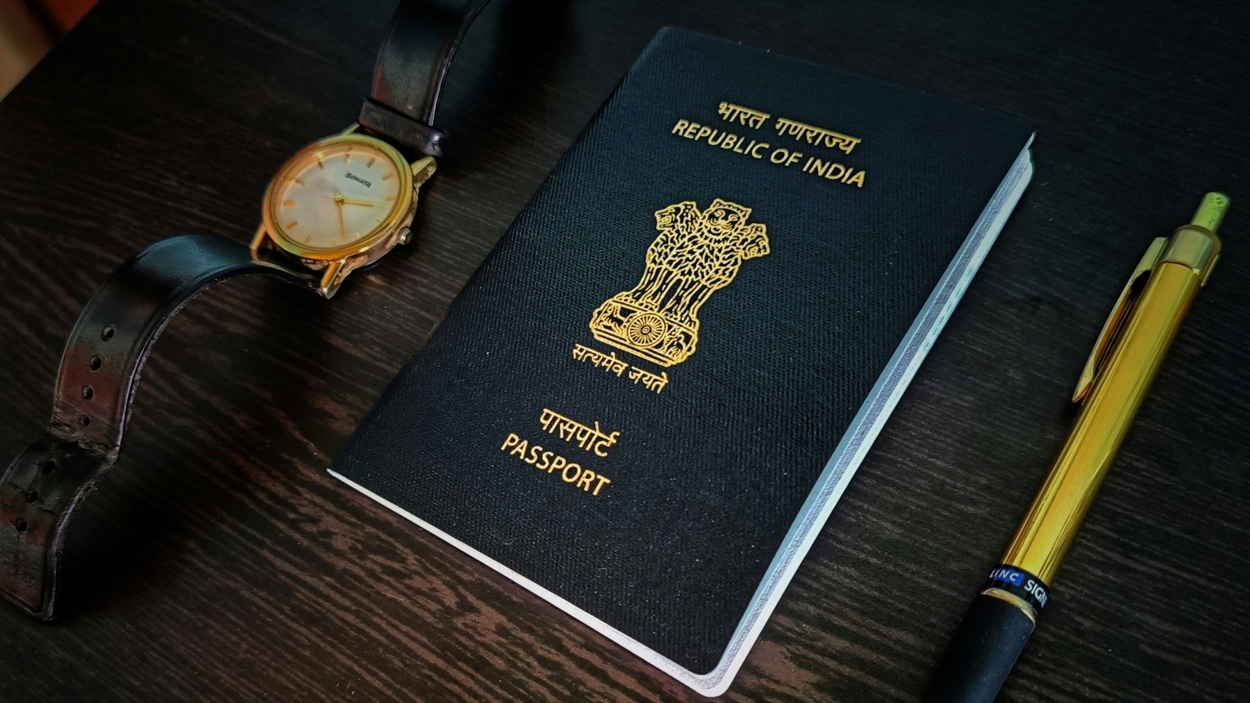 Indian passport on a wooden table next to a wristwatch and a pen, ready for a first international trip