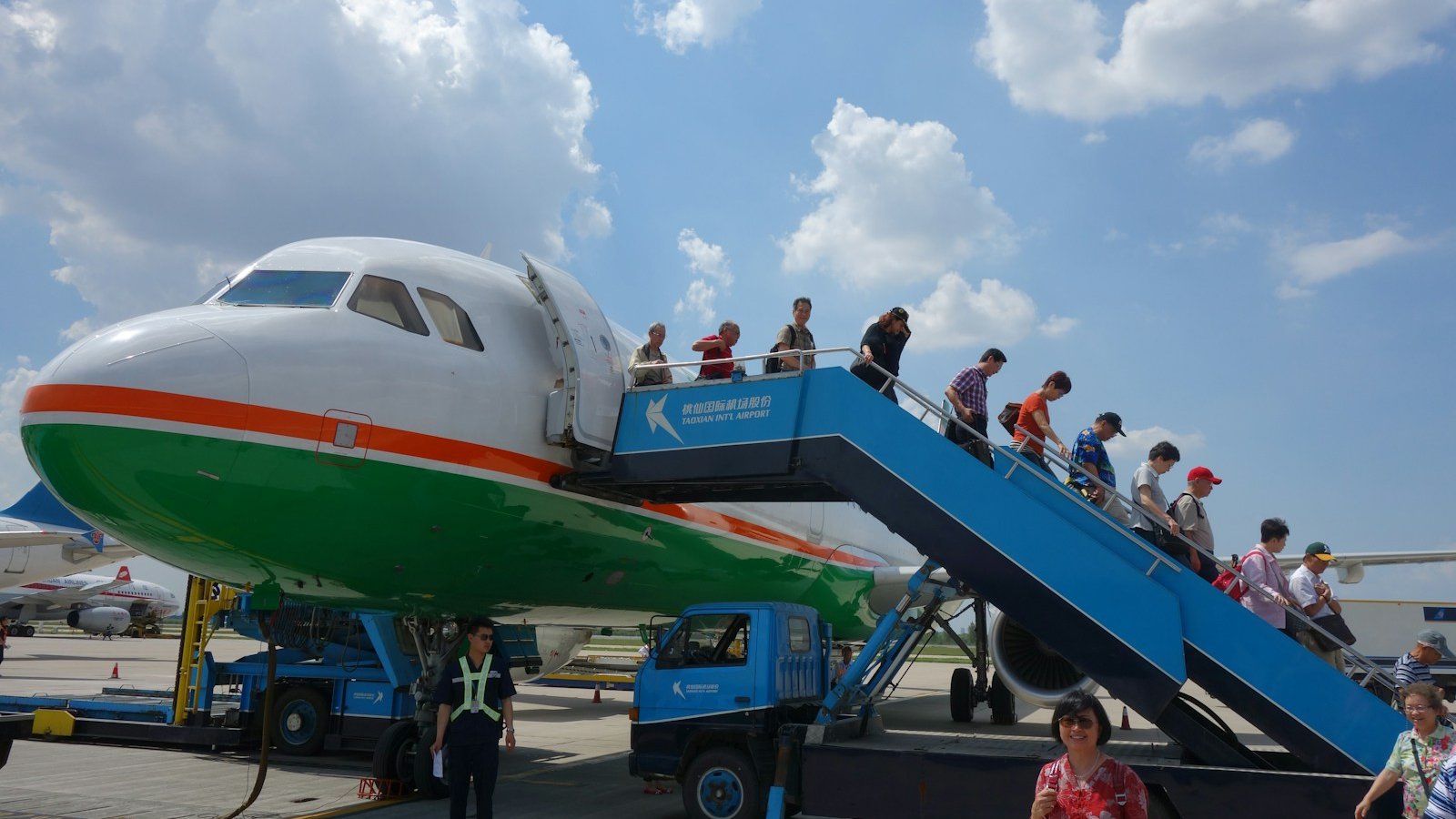 Passengers walking down mobile boarding stairs from a narrow-body jet parked on an airport apron
