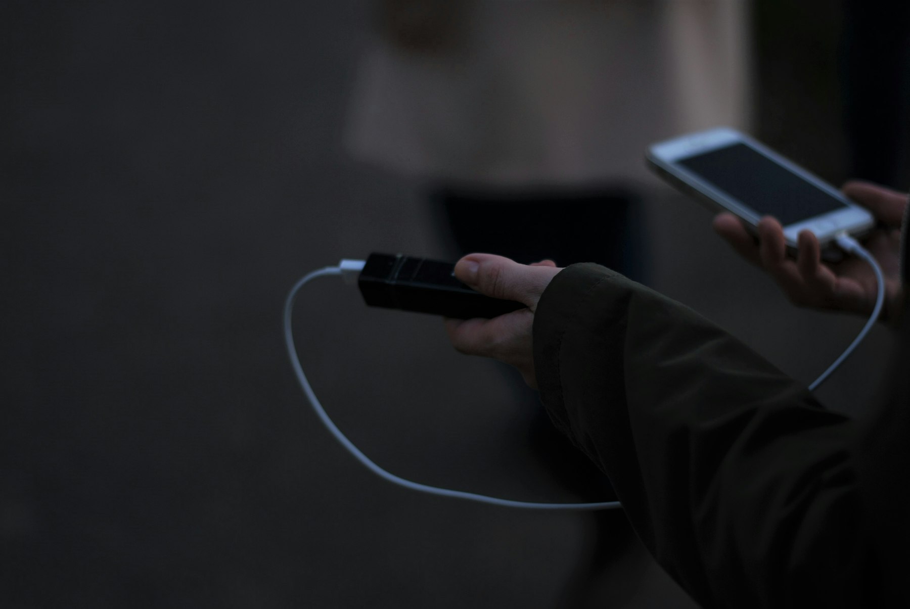 Traveler holding a small black power bank connected to a smartphone by a white cable