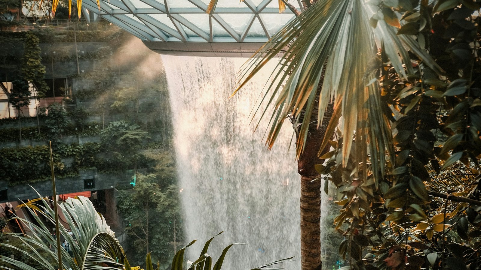 Rain Vortex waterfall under the glass dome at Jewel Changi Airport, Singapore, framed by palm trees