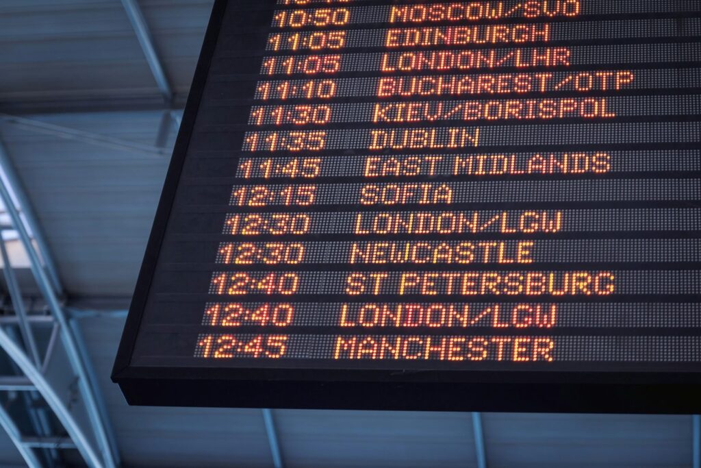 Airport departure board listing flight times and destinations in orange lights