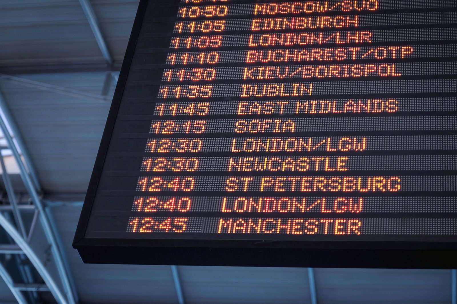 Airport departure board listing flight times and destinations in orange lights